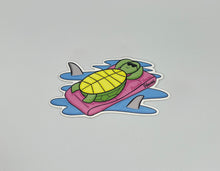 Load image into Gallery viewer, Turtle Sticker: hand-drawn sea turtle in sunglasses lounging on a pink float with shark fins in blue water